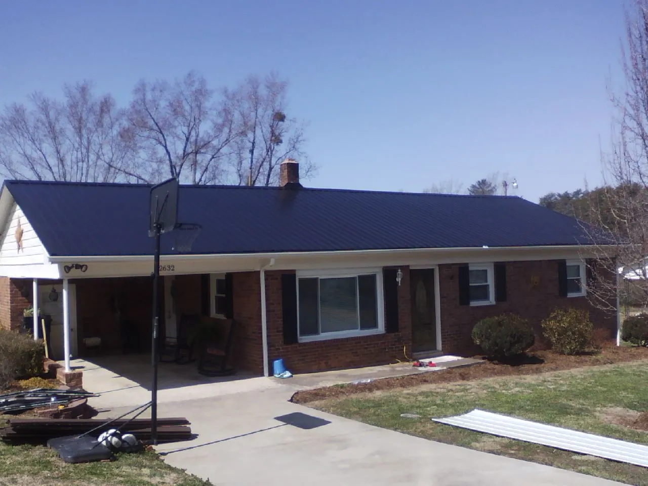 Finished dark blue metal roof on a brick ranch with a carport in Asbury