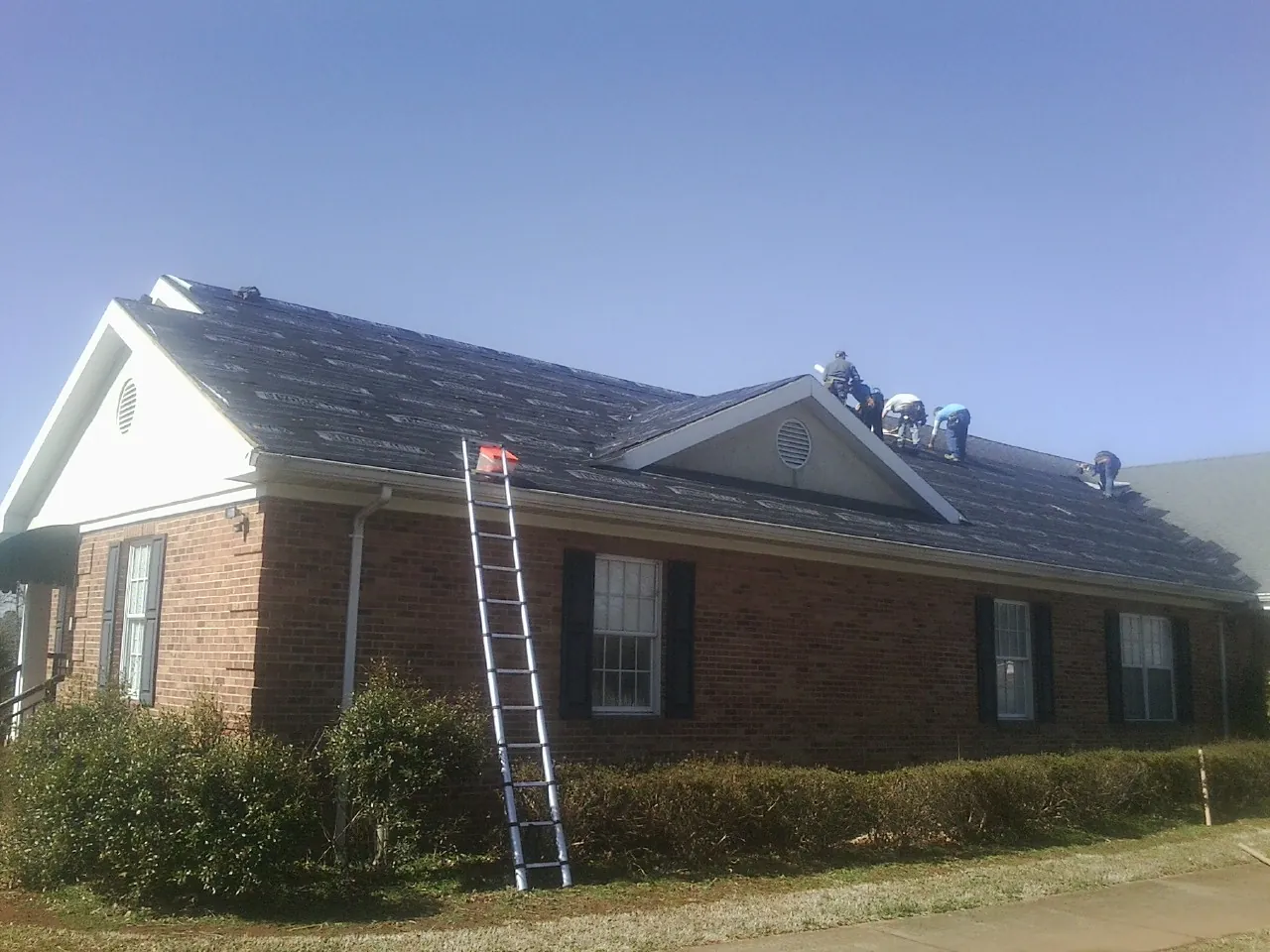 Crew tearing shingles off a brick ranch roof with a ladder set — Metal Roof Repair work by our crew in Asbury
