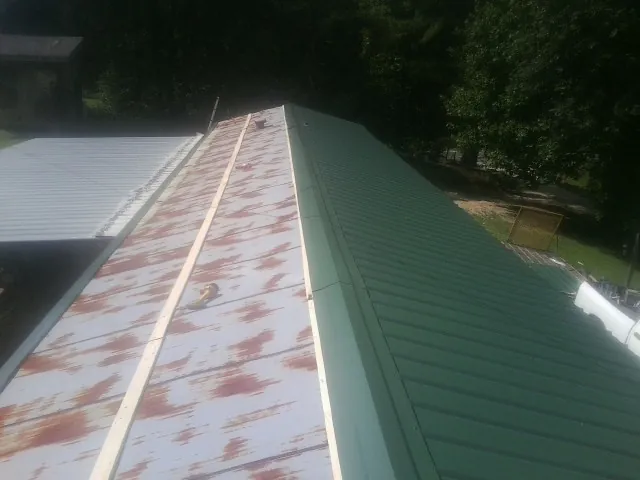 Old rusted panels beside newly installed green metal roofing — Wind Damage Roof Repair by Roofing Brothers in Asbury