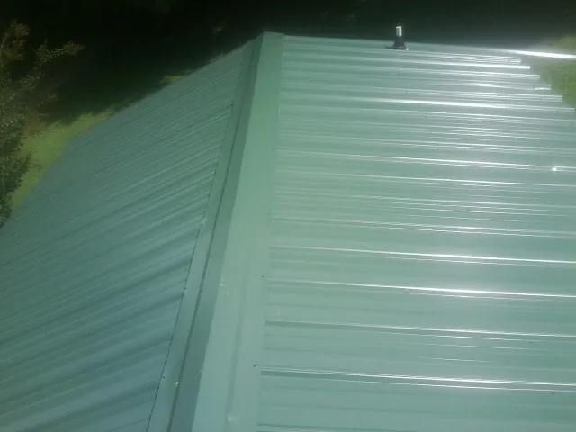 New green metal panels meeting at the ridge of a roof — Flat Roof Repair work by our crew in Asbury
