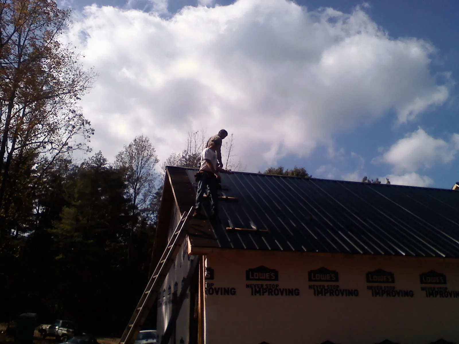 Roofer fastening dark metal panels high against a cloudy sky, from a Roof Inspection job in Asbury