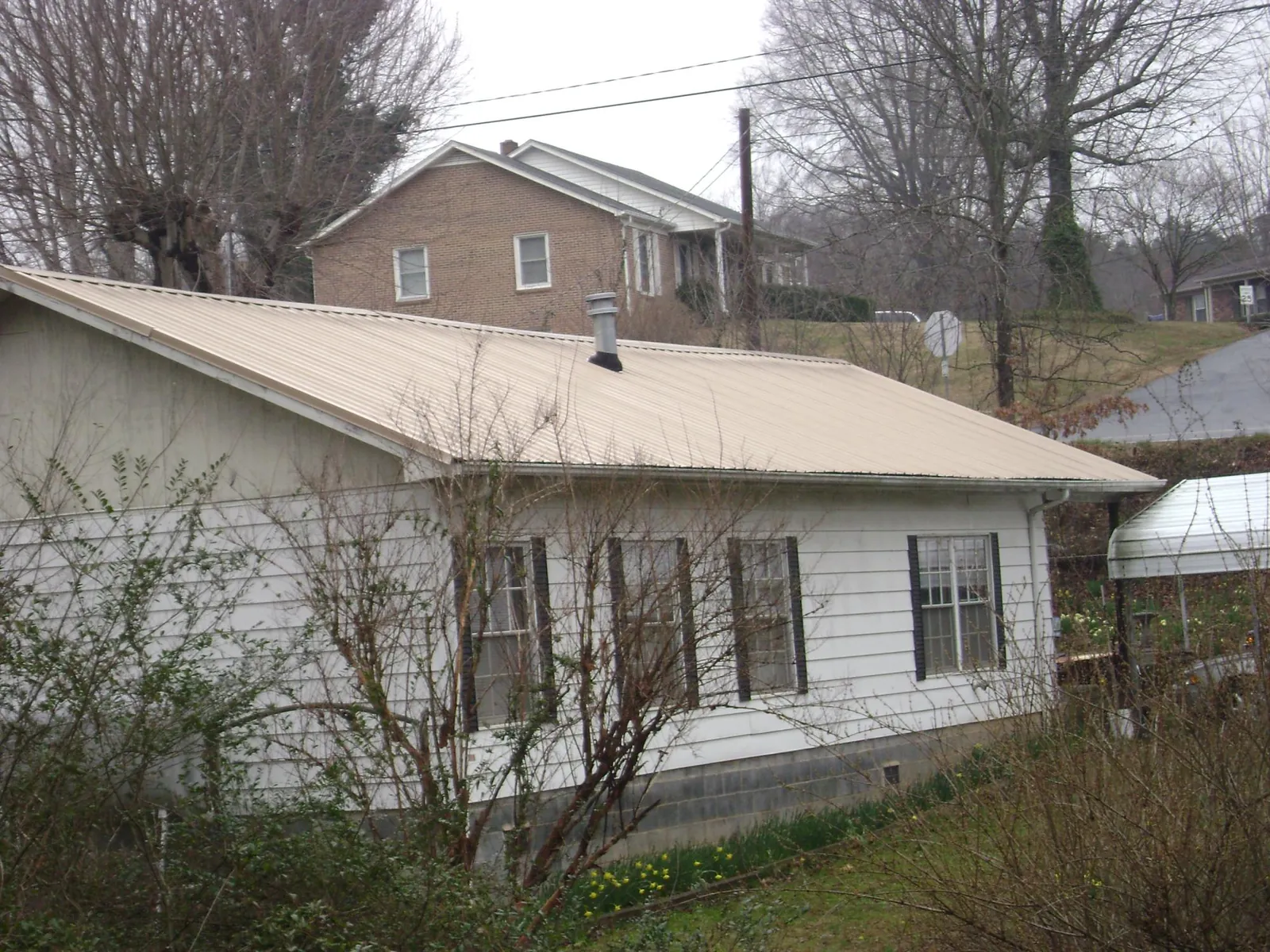 Tan metal roof on a white sided house set into a hillside — Commercial Roofing by Roofing Brothers in Asbury