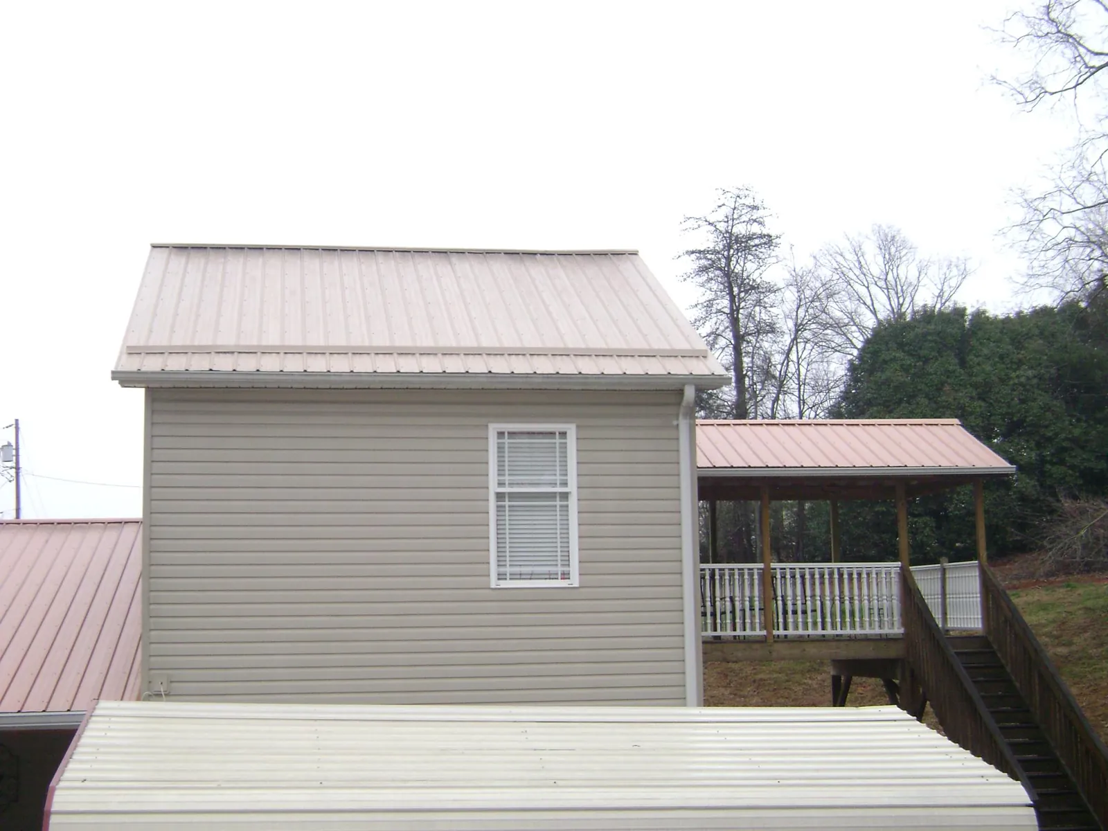 Tan metal roofs on a two story addition and attached porch, from a Roof Replacement job in Asbury
