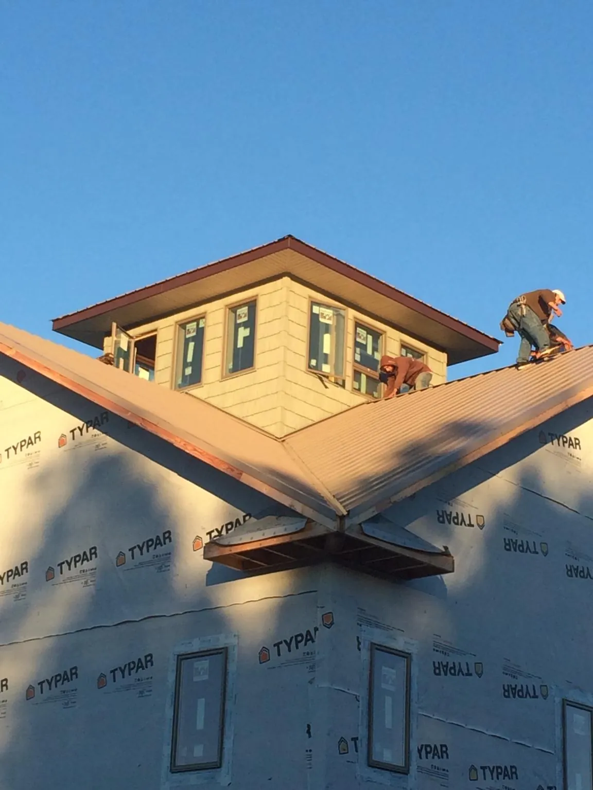 Roofers working around a rooftop cupola on a new metal roof at sunset — Roof Waterproofing in Asbury by Roofing Brothers